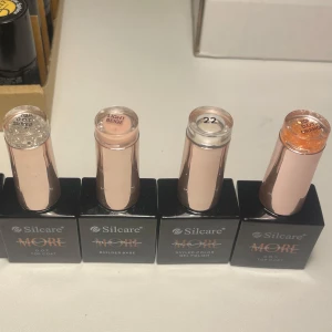 Silcare nagellack och builder base - Fyra flaskor nagelprodukter från Silcare. Inkluderar två top coats med glitter (ett silver, ett orange), en builder base i ljus beige och en universal gel polish i silver. Flaskorna har svart botten och roséguldfärgade lock.