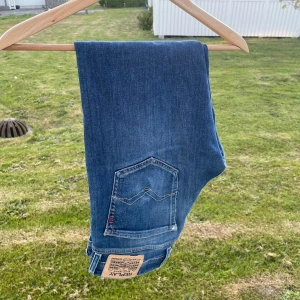 Blå Replay jeansbyxor - Säljer ett par klassiska blå jeans från Replay med fem fickor och snygga detaljer på bakfickan. Byxorna har normal passform och är tillverkade i ett mjukt denimty. Perfekta för dig som gillar stilrena och bekväma jeans.