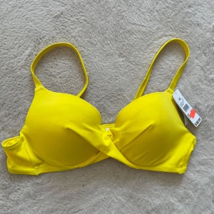 Gul bikiniöverdel push up  - Säljer en neon-gul push up bikiniöverdel från Cubus i storlek 40. Modellen har justerbara axelband och klassisk knäppning bak. Perfekt för dig som vill ha en färgstark look på stranden!