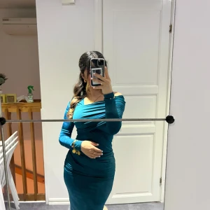 Turkos offshoulder klänning - Säljer en snygg turkos klänning med offshoulder-design och lång ärm. Klänningen har en tight passform och markerar midjan på ett smickrande sätt. Perfekt för dig som vill sticka ut med färg och stil.