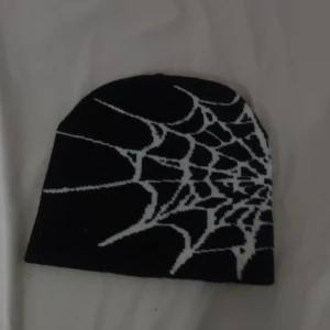 Svart mössa med spindelnätsmönster - Cool svart mössa med vitt spindelnätsmönster på båda sidorna. Perfekt för dig som gillar unika accessoarer med lite edge. Mjuk och stretchig passform som sitter skönt på huvudet.