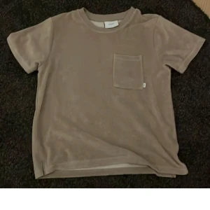 Beige frotté t-shirt från Grunt - Säljer en beige t-shirt från Grunt i mjuk frotté med bröstficka. Perfekt för en avslappnad stil och skön att ha på sig under varmare dagar. Klassisk passform och rund halsringning.