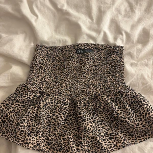 Leopardmönstrad kortkjol från ZARA - Supersnygg kortkjol från ZARA med leopardmönster. Kjolen har smock i midjan för en bekväm passform och volang nertill som ger extra rörelse. Perfekt för dig som vill sticka ut lite extra!