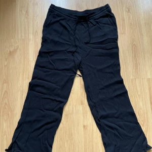 Svarta byxor - Svarta byxor med dragsko i midjan. Byxorna har en avslappnad passform och raka ben, perfekta för en chill vardagslook. Storlek L men har justerbar midja så passar mindre storlekar.