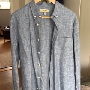 Blå skjorta från Whyred - Snygg blå skjorta från Whyred med diskret vävt mönster. Skjortan har klassisk krage, vita knappar och en bröstficka. Perfekt för dig som gillar stilrena plagg med en modern touch. Helt oanvänd, fick i present men fel storlek för mig.