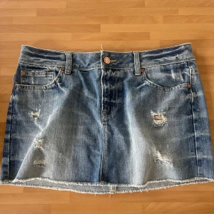 Blå jeanskjol från Gina - Perfect Jeans - Säljer en blå jeanskjol från Ginatricot Perfect Jeans i storlek M. Kjolen har slitna detaljer, rå kant nertill och klassiska fickor både fram och bak. Perfekt för dig som gillar en avslappnad och trendig stil.