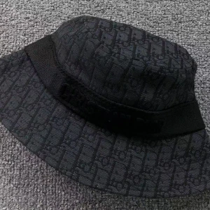 Svart bucket hat från Christian Dior - Säljer en svart bucket hat från Christian Dior med diskret mönster och broderad logga runtom. Hatten har bred brätte och är tillverkad i ett tyg med struktur. Perfekt accessoar för en trendig look.