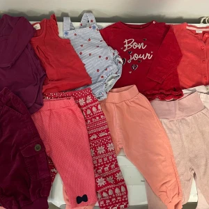 Klädpaket flicka storlek 80 - 11 plagg. Flera par mjuka byxor i olika rosa och röda nyanser. Ett par har juligt mönster i rött och vitt, ett par är enfärgat ljusrosa och ett par är korallrosa med rosett. Perfekta för lek och vardag. Allt för 100:-