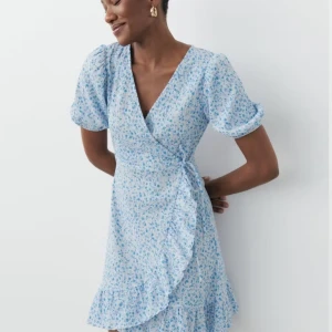 Sommar klänning - Supersöt ljusblå omlottklänning med små blommor, puffärmar och volangkant. Knyt i midjan och v-ringad framtill. Perfekt för vår/ sommar/ skolavslutning, köptes ny och har bara prövats på en gång🎀 Stretchigt och lätt material.