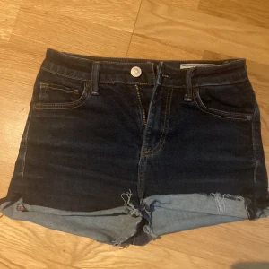 Mörkblå jeansshorts från Crocker - Snygga mörkblå jeansshorts från Crocker med klassisk femficksdesign och råa, uppvikta benslut. Modellen är högmidjad och har knapp- och dragkedjestängning. Perfekta för varma dagar och enkel att matcha med olika toppar. Går att vika upp som man vill. Som som gått upp bak, se bild.