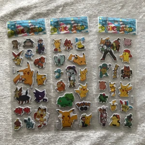 Pokémon klistermärken - Tre ark med färgglada Pokémon-klistermärken. Motiven inkluderar Pikachu, Bulbasaur, Charmander, Squirtle, och flera andra populära Pokémon samt tränare. Klistermärkena är i olika former och storlekar, med tydliga konturer och glada färger. Perfekt för att dekorera anteckningsböcker eller datorer. 45kr/3st/bild, samma frakt om du köpa båda  3år + 