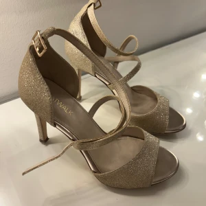 Glittriga klackskor - Säljer ett par glittriga Klackskor i guld från Catwalk med öppen tå och smal klack. Skorna har justerbart spänne vid ankeln och breda remmar över foten. Använda ett fåtal gånger, dom är lite smutsiga under skon alltså på sulan.🌸💕