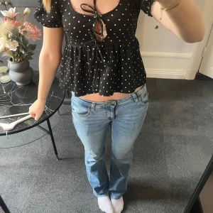 Svart prickig croppad blus med knyt - Superfin svart blus med vita prickar och korta puffärmar. Toppen är croppad och har en söt knytning framtill samt volang nedtill. Perfekt för sommardagar och ger en trendig look.