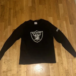 Svart långärmad tröja Supreme x NFL Raiders - Svart långärmad tröja från Supreme i samarbete med NFL och Raiders. Tröjan har Raiders-logga på bröstet och Supreme-brodyr på ärmen. Tillverkad i bomull med en strukturerad, lite tjockare känsla. Perfekt för dig som gillar streetwear och sport.