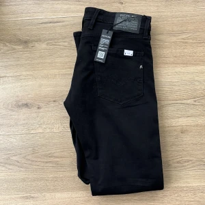Helt nya Svarta Replay jeansbyxor herr - Säljer ett par svarta Replay jeansbyxor i modell Anbass. Byxorna har klassisk femficksdesign, raka ben och normal passform. Materialet är stretchigt och bekvämt, perfekt för en stilren look. Midjemått W34 och längd L32. Nypriss 1599 mitt endast 550.