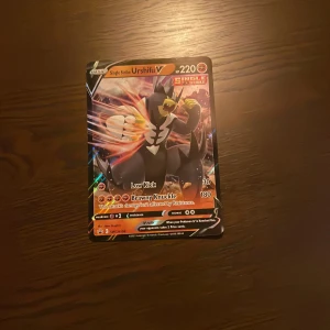 Pokémonkort Single Strike Urshifu V - Säljer ett Pokémonkort: Single Strike Urshifu V med 220 HP. Kortet har en färgstark design med Urshifu i svart och rött, och är en V-kortvariant med attacker som Low Kick och Brawny Knuckle. Perfekt för samlare eller spelare!