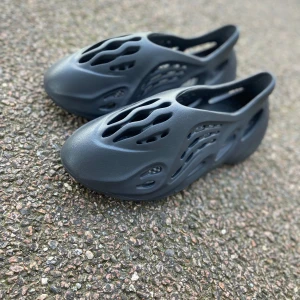 Adidas Yeezy Foam Runner i svart - Säljer ett par svarta Foam Runner. Skorna har en futuristisk design med många hål och är tillverkade i syntetmaterial. Perfekta för dig som vill ha något unikt och bekvämt på fötterna. Ingen låda