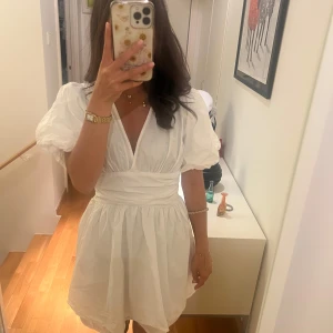 Vit kortklänning med puffärmar - Superfin vit kortklänning med puffiga kortärmar och omlott-v-ringning. Klänningen har markerad midja med knyt och lätt rynkad kjol. Perfekt för student, konfirmation, skolavslutning eller någon av sommarens alla tillfällen. Storlek S!💕