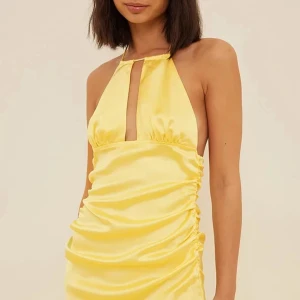 Gul halterneck klänning från NA-KD by Misslisibell - Säljer en snygg gul halterneck klänning från NA-KD i satin med öppen rygg och kort längd. Klänningen har en smickrande passform och en snygg detalj framtill med slits vid bysten. Perfekt för sommarens alla tillfällen!