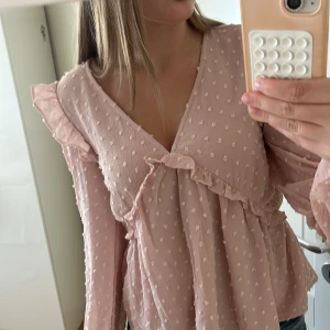 Söt ljusrosa blus - Söt ljusrosa blus med volangdetaljer vid V-ringningen. Helt ny med prislappen kvar! Perfekt för både vardag och fest. Långärmad och lättmatchad. Säljes på grund av felköp. Storlek 170, material. Fler bilder kan skickas vid förfrågan. Passa på att fynda!
