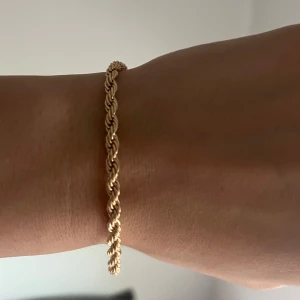 Cordell armband i guldfärg - Snyggt armband i tvinnad design/cordell med guldfärg. Justerbar längd med kedja och karbinlås. Kan justeras från 16cm-21cm.