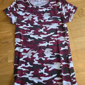 Kortärmad t- shirt med kamouflagemönster - Säljer en cool kortärmad t-shirt med kamouflagemönster i vinrött, svart, grått och vitt. Rund halsringning och rak passform. Perfekt för dig som vill sticka ut med en unik stil.
