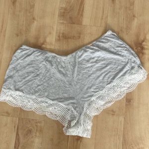 Grå shorts med spetskant - Mjuka grå shorts med bred vit spets längs bensluten. Lätta och bekväma med lös passform, perfekta för varma dagar eller som mysplagg hemma.