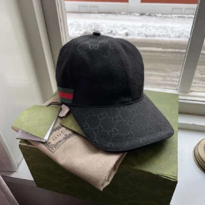 Svart keps från Gucci - Snygg svart keps från Gucci med diskret GG-mönster och klassiska gröna och röda ränder på sidan. Kepsen har böjd skärm och justerbar passform. Perfekt accessoar för en trendig look.