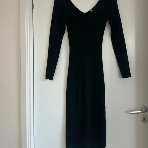 Svart långklänning med v-ringning - Säljer en elegant svart långklänning med djup v-ringning både fram och bak. Klänningen har lång ärm och en figurnära passform som framhäver siluetten. Perfekt för dig som vill ha en stilren och tidlös look. Oklart vilken storlek men passar både 34/36