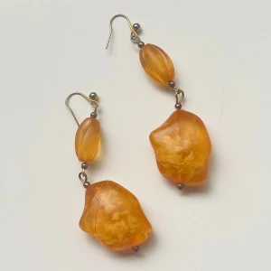 Orange statement örhängen med oregelbunden form - Säljer ett par unika orange örhängen med stora, oregelbundna pärlor i troligen bärnsten . De har en varm, bärnstensliknande färg och hängs på krok. Perfekta för att ge din outfit en färgklick!