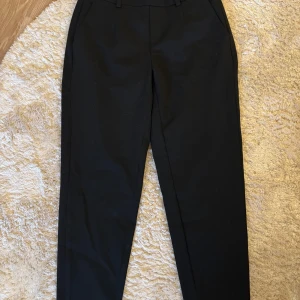 Svarta chinos från Object - Svarta chinos från Object med normal passform och resår i midjan. Byxorna har snedställda fickor fram och dekorativa fickor bak. 