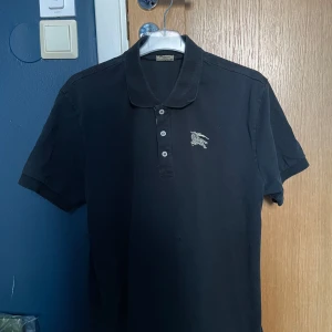 Svart pikétröja från Burberry - Säljer en svart pikétröja från Burberry. Knappt använd och perfekt för sommarkvällar. Även om det står XL så sitter den som en M. Nypris ligger på runt 2000-3000kr. Skriv gärna vid frågor, pris går att diskuteras.