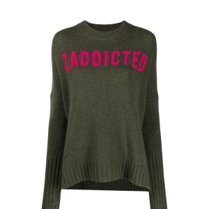 Olivgrön stickad tröja från Zadig & Voltaire - Säljer en olivgrön stickad tröja från Zadig & Voltaire i nyskick med texten 'ZADDICTED' i rosa framtill. Tröjan är tillverkad i 100% merinoull, har långa ärma, ribbade muddar och en något lös passform. Perfekt för dig som gillar statement-plagg. Liten defekt i handen (bild 5), men inget stort!💗