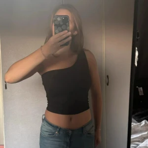 Svart one shoulder topp från Gina Tricot - Säljer en svart one shoulder topp från Gina Tricot. Toppen har en asymmetrisk design med en axel och är tillverkad i ett stretchigt material som sitter tight mot kroppen. Perfekt att styla med jeans eller kjol.☺️ (Har även en exakt likadan i vit om det skulle vara intressant)💕