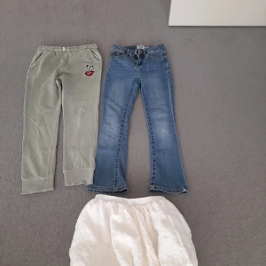 Grå mjukisbyxor, blå bootcut jeans och vita fluffiga byxor - Två par byxor: ett par grå mjukisbyxor med tryckdetaljer, ett par blå bootcut jeans och en vit kjol Perfekta för olika tillfällen och stilar.