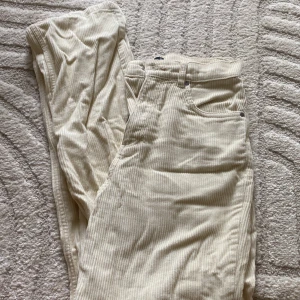 Beiga manchesterbyxor från Gina Tricot - Säljer ett par beiga manchesterbyxor från Gina Tricot. Byxorna har hög midja, raka ben och klassiska fickor både fram och bak. De är tillverkade i mjuk manchester och har dragkedja och knapp framtill.