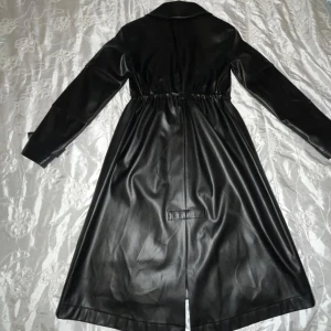 Svart lång skinnjacka - Säljer en svart lång skinnjacka med bälte i midjan och klassisk krage . Jackan har långa ärmar och är helfodrad på insidan för extra komfort.Nytt pris (1900kr)Perfekt för dig som vill ha stilen .Köpt i Antalya 