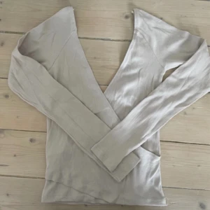 Beige omlottopp - Snygg beige/grå omlottopp med lång ärm och v-ringad design. Perfekt för en stilren look.