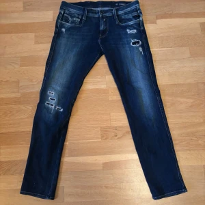 Mörkblå Replay jeans med slitningar - Säljer ett par mörkblå Replay jeans i modell Anbass, storlek 29/30 men skulle säga att som sitter som 28/30. Skick: 10/10 endast använda fåtal gånger. Hör av dig om du har frågor!
