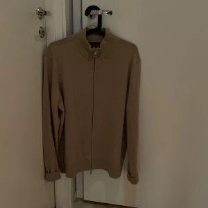 Morris kofta i kashmir och merinoull  - Säljer en beige stickad kofta från Morris med hel dragkedja framtill och hög krage. Tröjan har långa ärmar och ribbade muddar vid ärmslut och nederkant. Det är kashmir och merinoulls material på tröjan. Tröjan kostar i nypris 3.000kr. Perfekt när de blir lite kyligare ute en sommarkväll! Hör av er vid fler frågor.