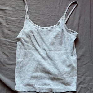 Grå ribbad linnetopp - Säljer en enkel och stilren grå ribbad linnetopp med smala axelband. Perfekt att matcha med jeans eller kjol för en avslappnad look.