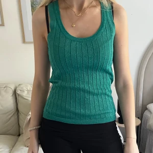 Grön glittrig topp - Säljer en grön glittrig linnetopp med ribbat mönster. Perfekt för fest.