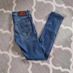 Blå slim jeans med klassisk femficksdesign - Säljer ett par blå slim fit jeans med klassisk femficksdesign och kontrastsömmar. Jeansen har normal midja och raka ben, tillverkade i denim med snygg tvätt. Passar perfekt till vardagslooken.