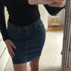 Jeanskjol Jane Skirt - Säljer en klassisk blå jeanskjol från Jane Skirt i storlek M. Kjolen är kort, har normal passform och typiska jeansdetaljer som fickor och synliga sömmar. Perfekt att styla med en enkel topp.
