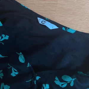 Svart blommig blus med knyt (S/M) - Supersöt svart blus med grönt blommigt mönster och v-ringning. Blusen har puffiga trekvartsärmar och ett snyggt knyt i midjan som ger en fin siluett. Perfekt för dig som gillar färg och mönster! Vill bara bli av med den, använd ganska mycket men det är inga defekter på den. Pris går att diskutera 