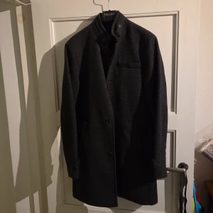 Rutig rock från Jack & Jones M - Snygg mörkgrå rutig rock från Jack & Jones Premium. Klassisk rak modell med ståkrage, knappar framtill och diskreta fickor. Tidlös design med fina detaljer vid ärmslutet. Perfekt för dig som vill ha en stilren och clean look.