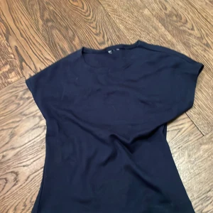 Mörkblå topp från Gina Tricot - En mörkblå topp från Gina Tricot med rund halsringning och korta ärmar. Toppen har en enkel och clean design som passar till många olika outfits. Storlek 134/140