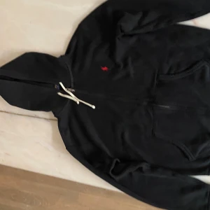 Svart hoodie från Ralph Lauren - Svart hoodie från Ralph Lauren med dragkedja och huva.