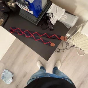 Onewear bälte! - Säljer ett svart bälte med röda sicksack-mönster och bruna skinn-detaljer vid ändarna. Bältet har en cool och unik design som sticker ut och passar perfekt till jeans eller chinos. Materialet är elastiskt och bekvämt.