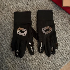 Svarta träningshandskar från Stanno - Svarta handskar från Stanno med vitt tryck och coolt geometriskt mönster på ovansidan. Handskarna har smidig passform och är perfekta för träning utomhus. Materialet känns syntetiskt och har stretchiga muddar för extra komfort.